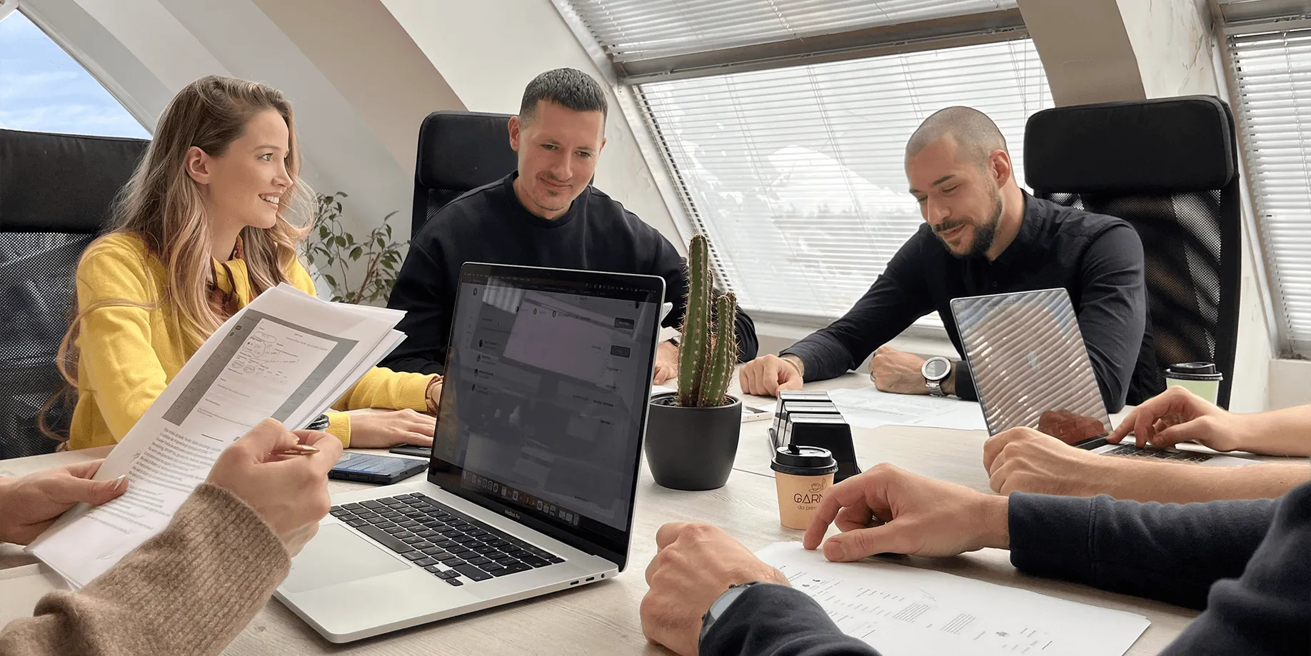 Five members of the Rationale team around a meeting table with laptops and printed documents in the Novi Sad office.