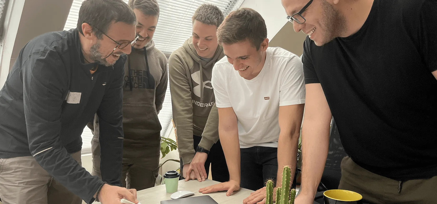 Six Rationale engineers standing around a desk in the Novi Sad office, working through a problem together.